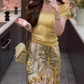 The queen is wearing a beautiful yellow short-sleeved T-shirt and floral skirt on vacation R0900